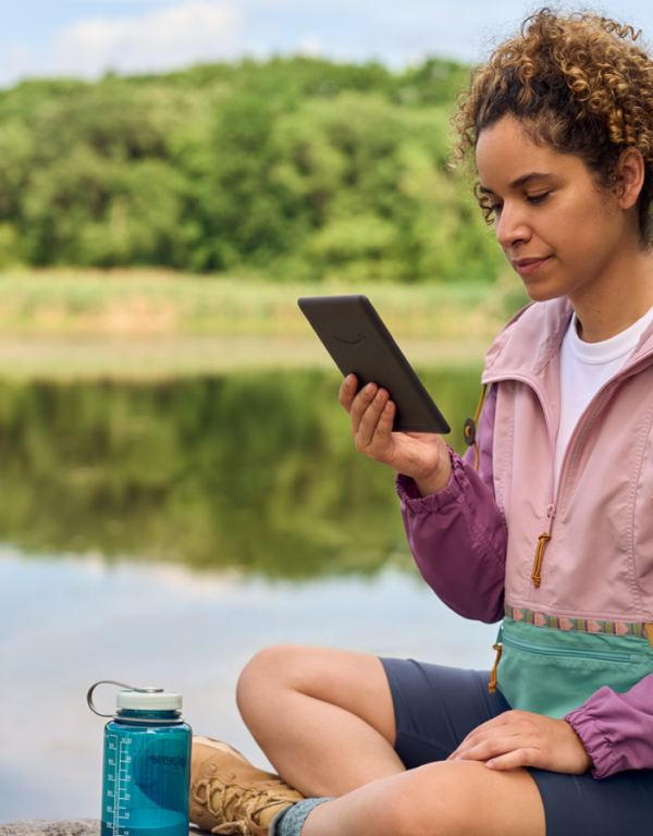 Kobieta czytająca ebooka na Kindle Paperwhite nad jeziorem.