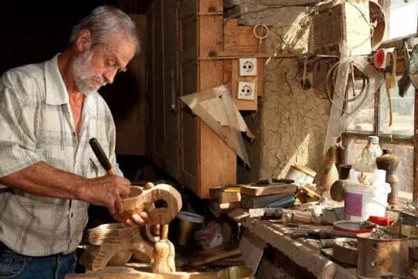 Starszy mężczyzna uprawiający snycerstwo, czyli rzeźbienie w drewnie, w swoim warsztacie.