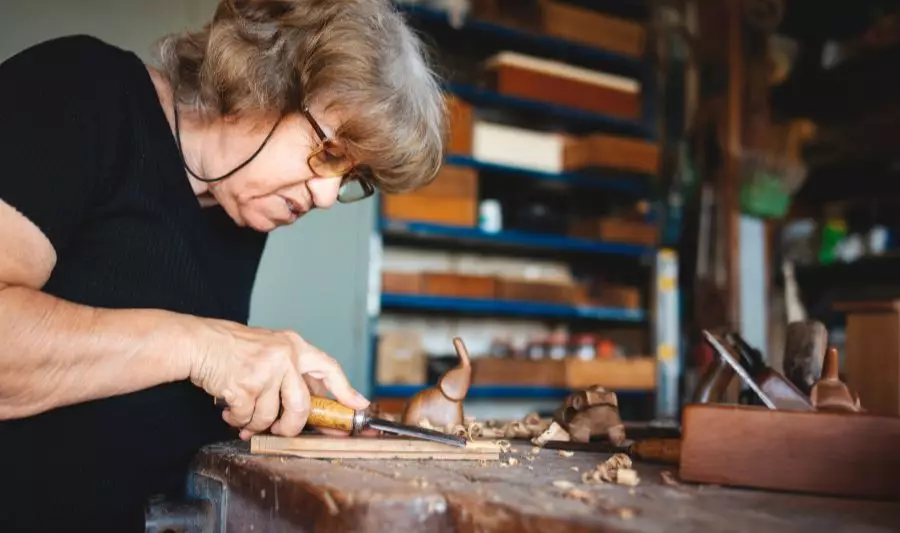Seniorka uprawia snycerstwo, czyli rzeźbienie w drewnie, w warsztacie.