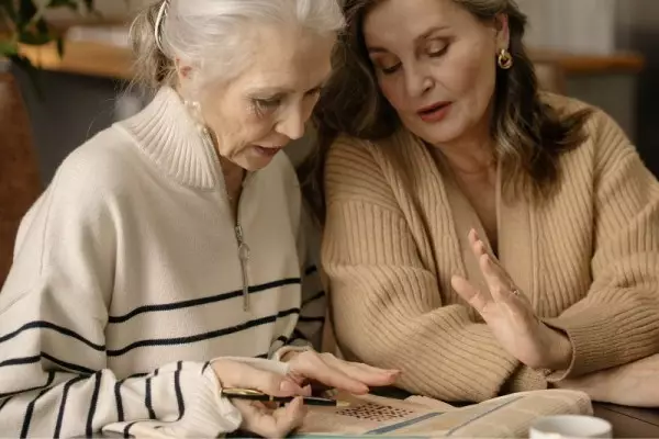 Dwie starsze kobiety rozwiązują łamigłówki dla seniorów w gazecie