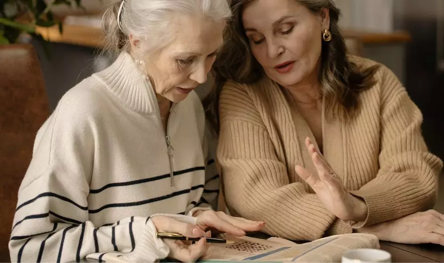 Dwie starsze kobiety rozwiązują łamigłówki dla seniorów w gazecie