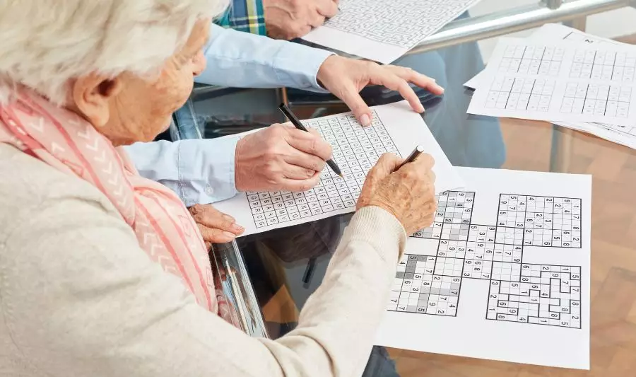 Starsza kobieta rozwiązuje łamigłówki dla seniorów w postaci gier sudoku.