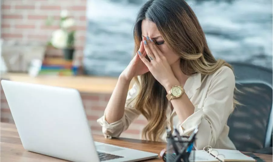 Kobieta po 50-tce odczuwa stres w pracy, siedząc przed komputerem.