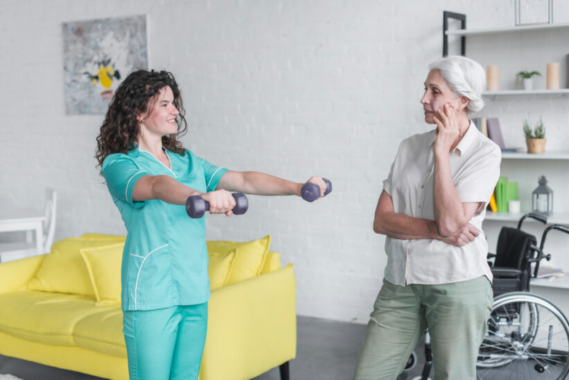 rehabilitantka pokazuje seniorce ćwiczenie z niewielkimi ciężarkami 