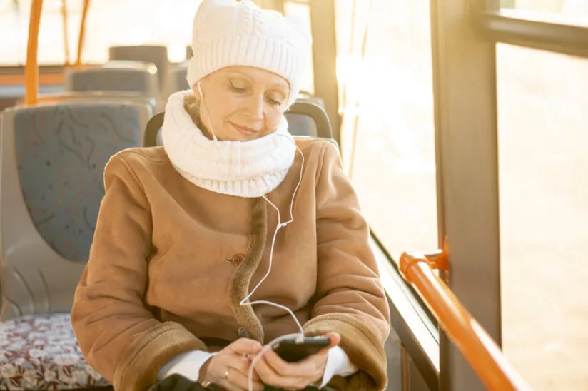 seniorka zamyślona jedzie w tramwaju, przegląda telefon i ma w uszach słuchawki 