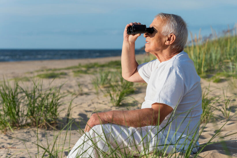 senior oglądający widoki nad morzem przez lornetkę 