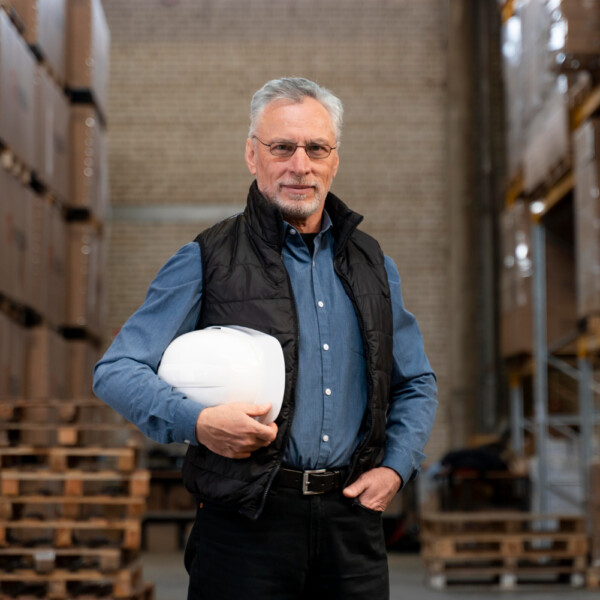 dojrzały mężczyzna pracujący w magazynie trzymający kask ochronny