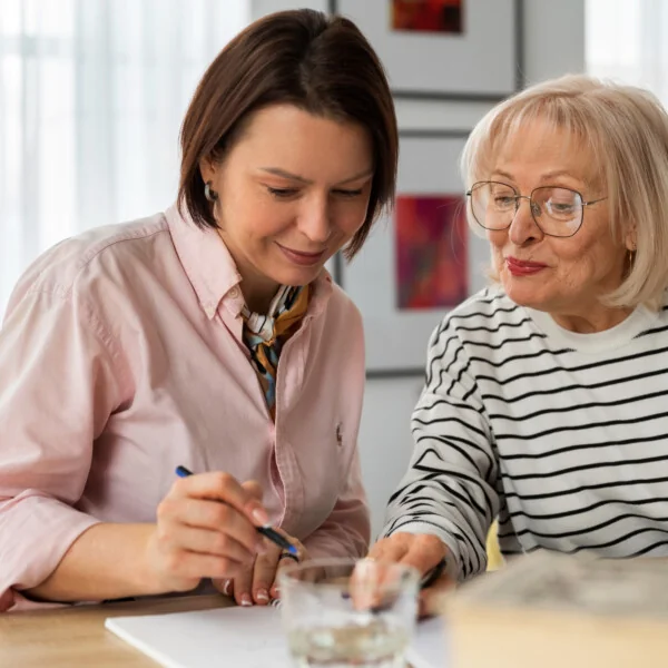 Opiekunka pomaga seniorce wypełnić dokumenty