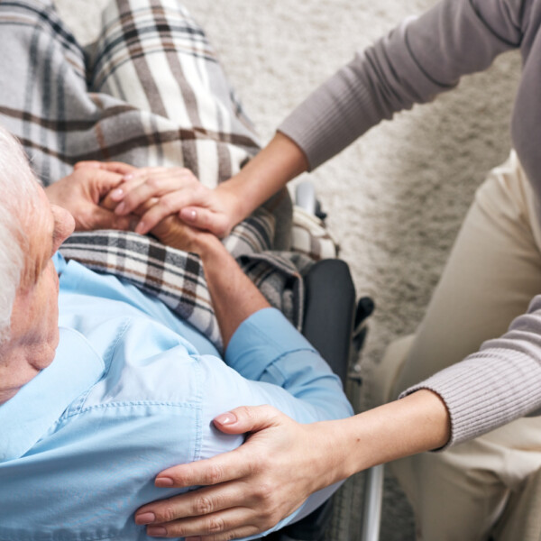 Opiekunka trzymająca za rękę seniora na wózku – codzienna opieka nad osobą starszą w domu