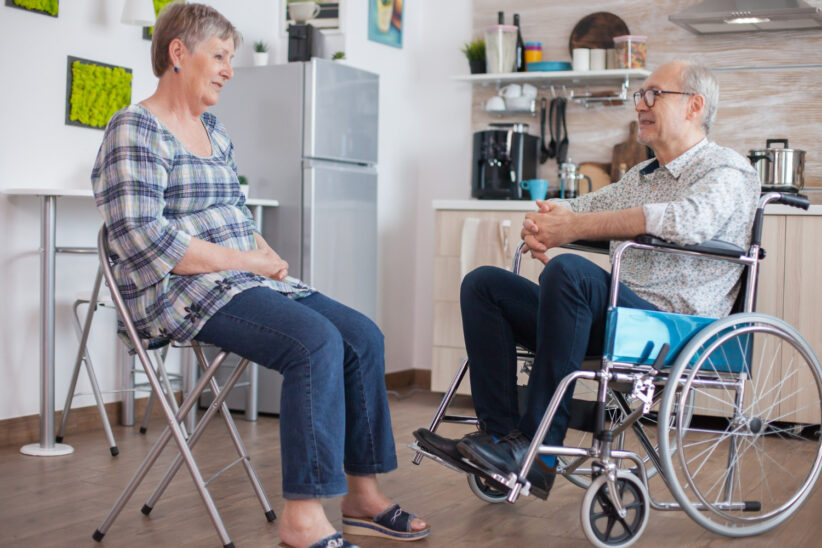 Senior na wózku rozmawia z seniorką na krześle 