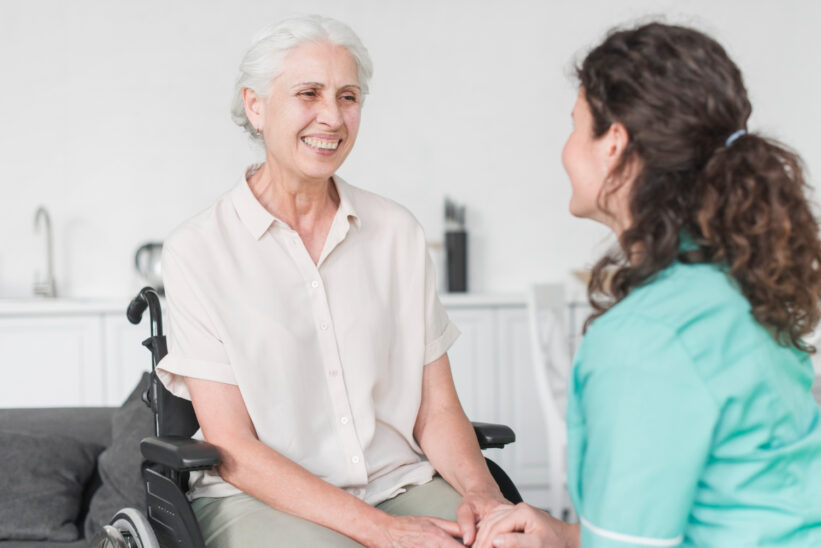 Seniorka na wózku rozmawiająca z opiekunką podczas domowej opieki długoterminowej