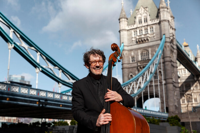 Muzyk z kontrabasem na tle Tower Bridge w Londynie – zagraniczna emerytura po pracy w Wielkiej Brytanii