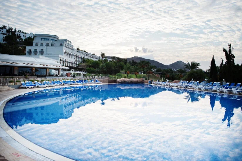 Basen przy hotelu uzdrowiskowym na tle gór i palm podczas spokojnego poranka.