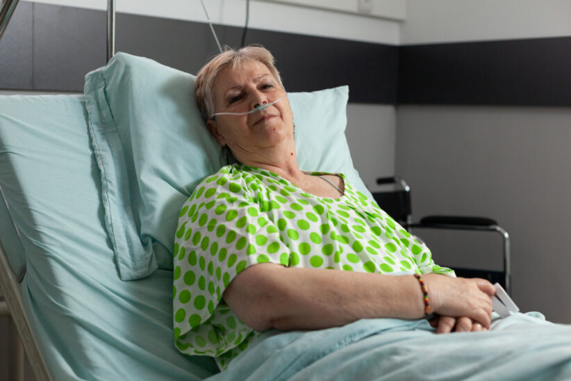 Seniorka leży w łóżku szpitalnym z założoną kaniulą tlenową