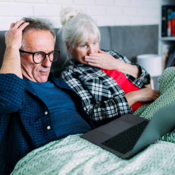 Zaniepokojona para seniorów leży w łóżku i patrzy na ekran laptopa.