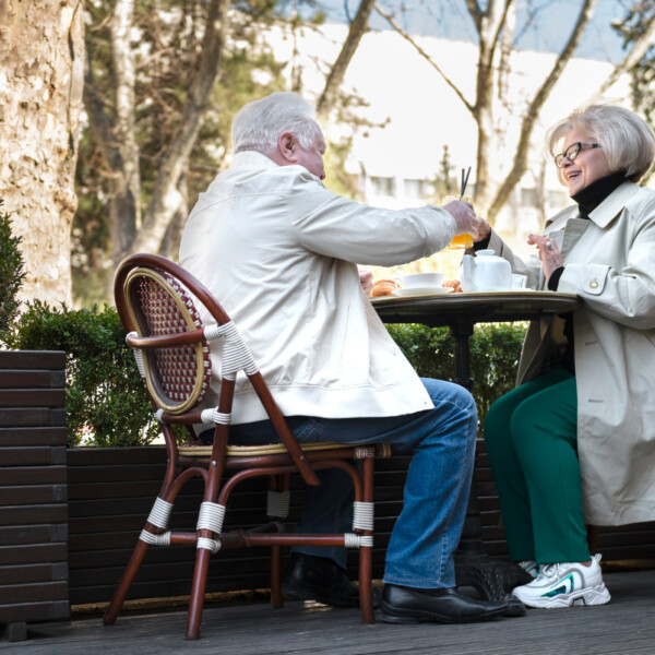 Seniorzy siedzą przy stoliku w kawiarni na świeżym powietrzu i rozmawiają podczas spotkania.
