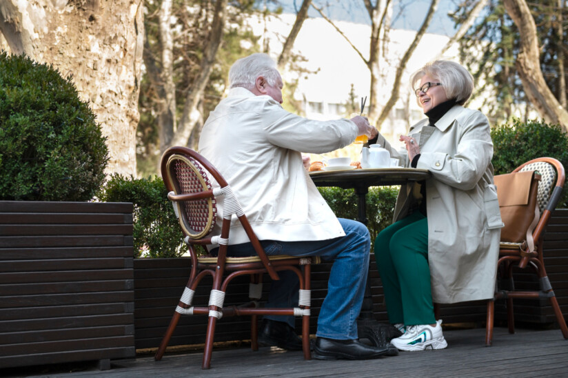 Seniorzy siedzą przy stoliku w kawiarni na świeżym powietrzu i rozmawiają podczas spotkania.