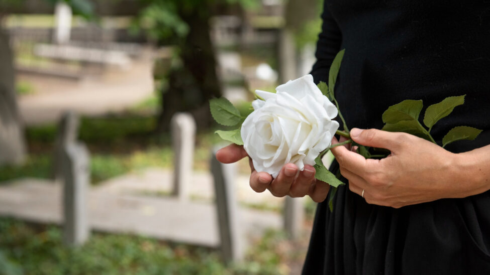 Osoba w żałobie trzymająca białą różę na cmentarzu