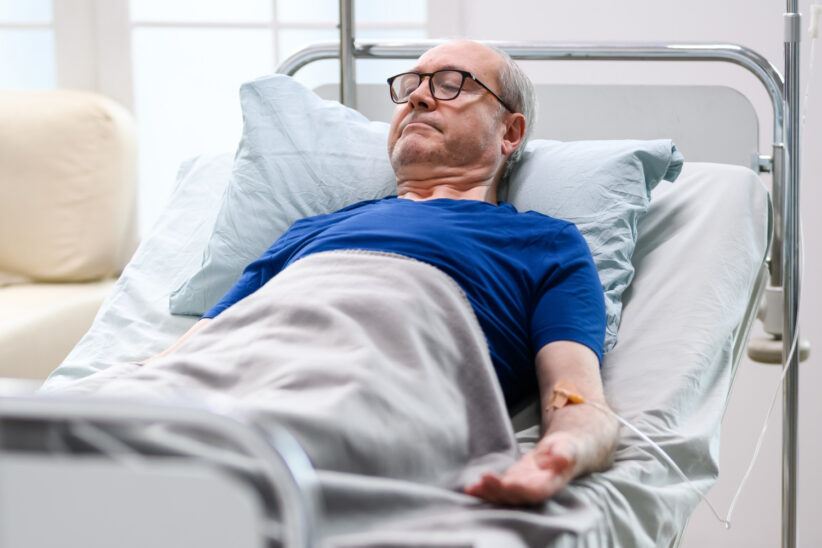 Senior leży w szpitalnym łóżku podłączony do kroplówki