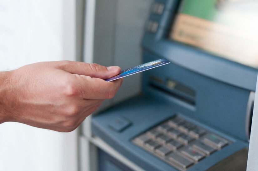 Dłoń wkłada kartę płatniczą do bankomatu podczas wypłaty gotówki.