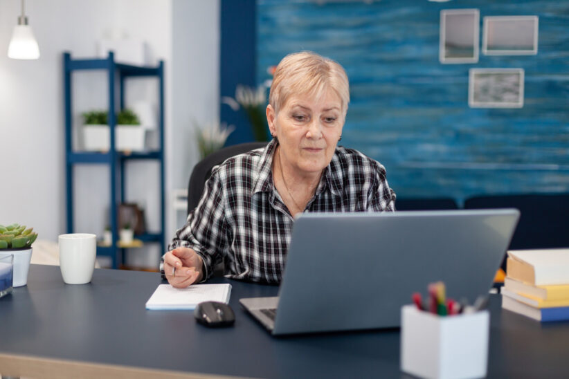 Seniorka pracująca przy laptopie i robiąca notatki