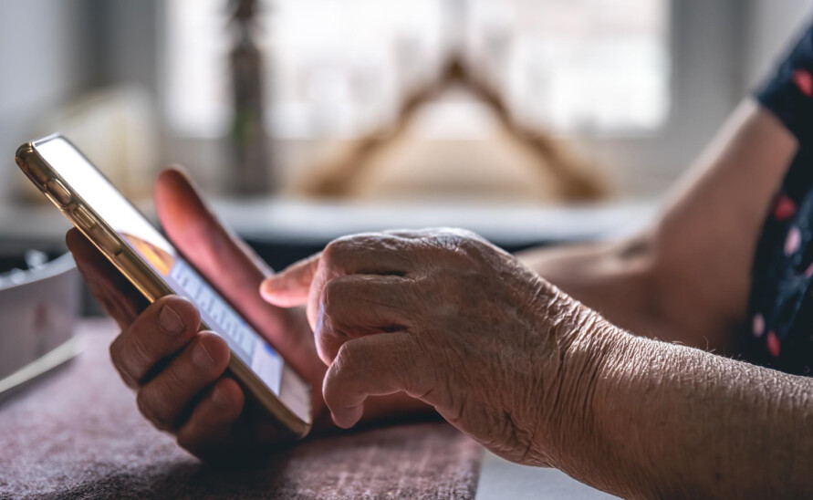 Smartfon w rękach seniora, czytającego SMS z fałszywym linkiem - oszustwo metodą na ZUS