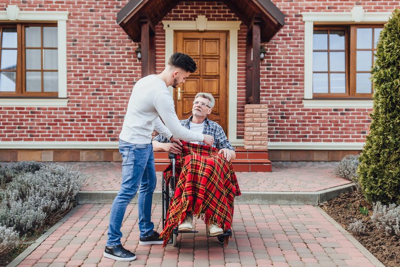 Syn opiekujący się ojcem na wózku, okrywa mu nogi kocem